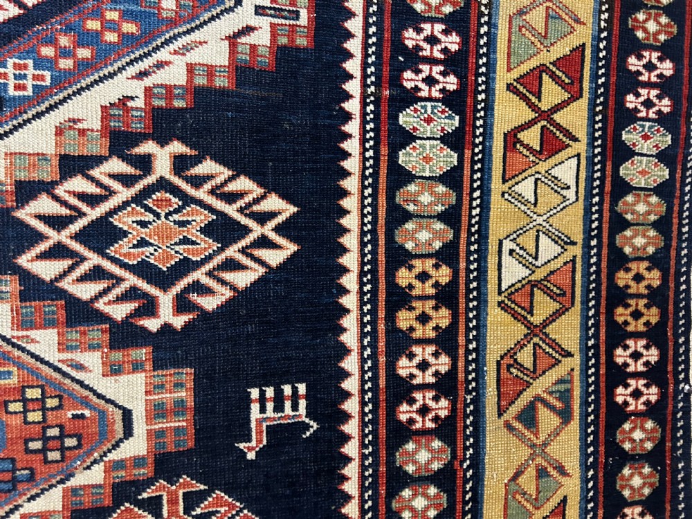 A rectangular hand-knotted wool rug displaying four diamond medallions along a navy central field surrounded by multi-tiered geometric borders. View XVI