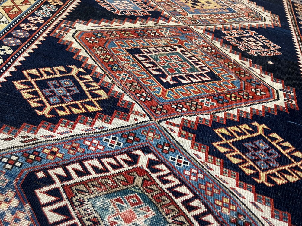 A rectangular hand-knotted wool rug displaying four diamond medallions along a navy central field surrounded by multi-tiered geometric borders. View XVII