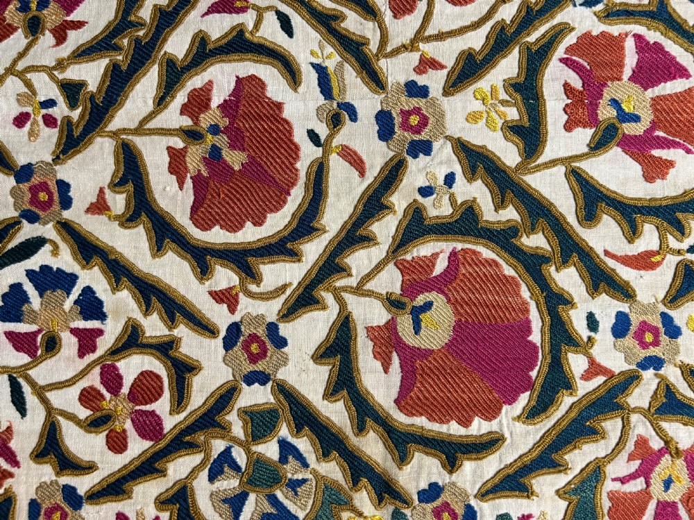 A rectangular silk embroidered suzani panel featuring terracotta red floral blossoms and dark green foliage on a cream woven ground. View II