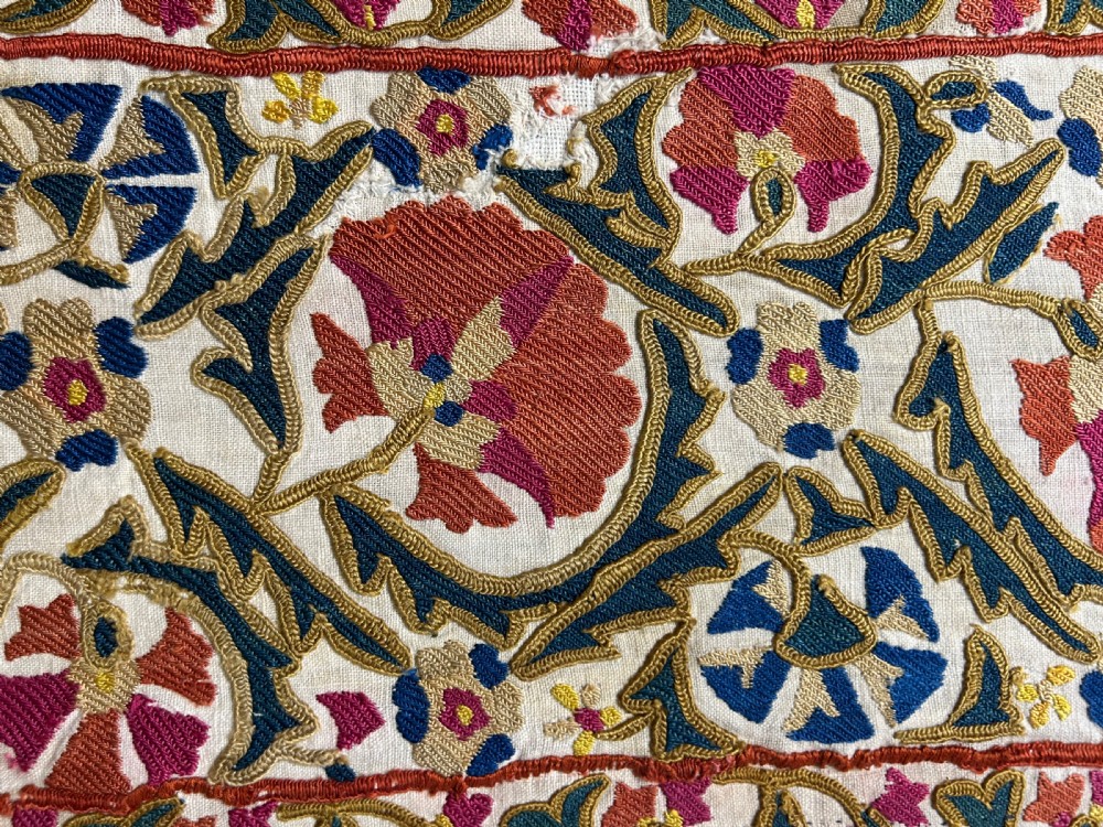 A rectangular silk embroidered suzani panel featuring terracotta red floral blossoms and dark green foliage on a cream woven ground. View III