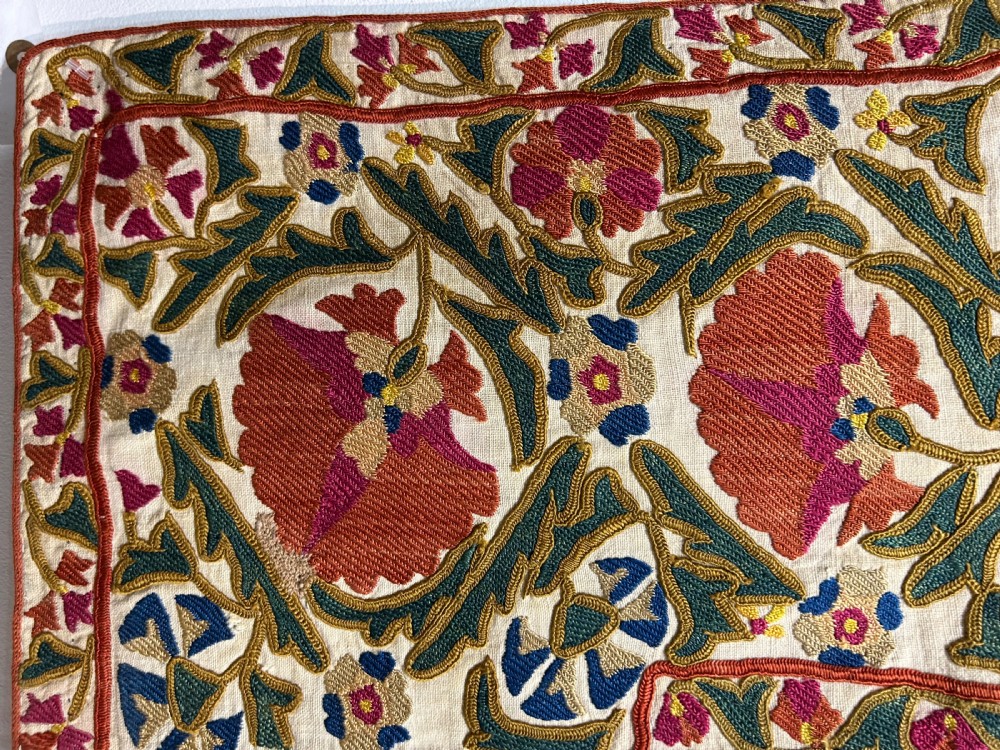 A rectangular silk embroidered suzani panel featuring terracotta red floral blossoms and dark green foliage on a cream woven ground. View IV