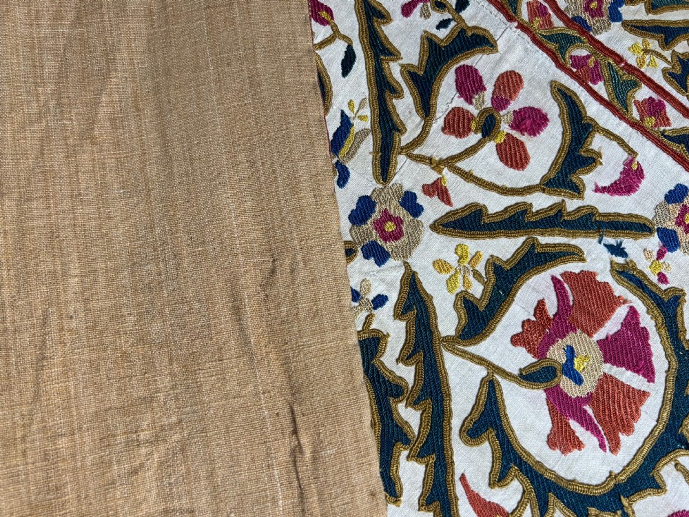 A rectangular silk embroidered suzani panel featuring terracotta red floral blossoms and dark green foliage on a cream woven ground. View VI