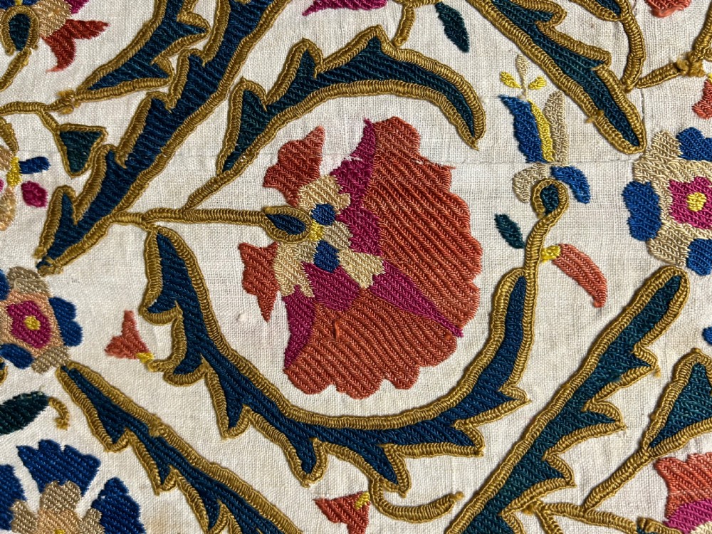 A rectangular silk embroidered suzani panel featuring terracotta red floral blossoms and dark green foliage on a cream woven ground. View VII