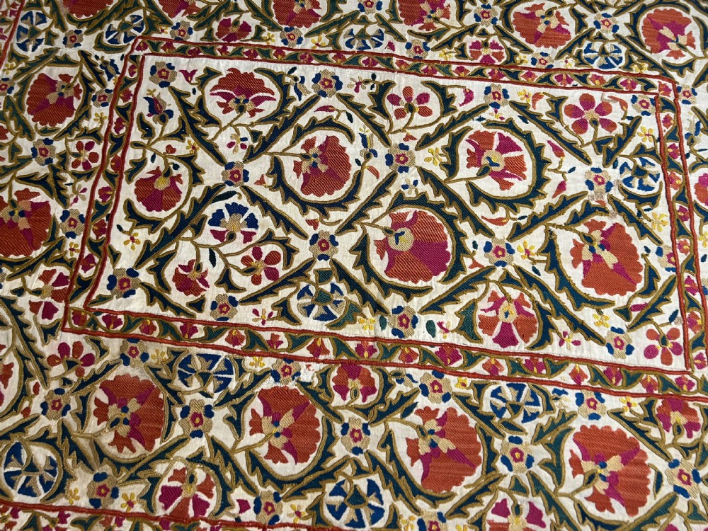 A rectangular silk embroidered suzani panel featuring terracotta red floral blossoms and dark green foliage on a cream woven ground. View VIII