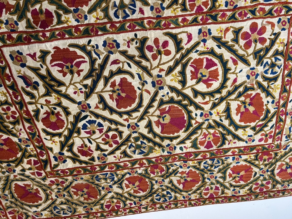 A rectangular silk embroidered suzani panel featuring terracotta red floral blossoms and dark green foliage on a cream woven ground. View IX