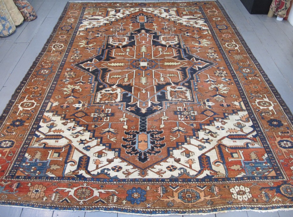 A large 19th-century antique Persian Serapi wool carpet featuring a bold geometric central medallion in navy blue and terracotta on an ivory field with wide decorative borders.
