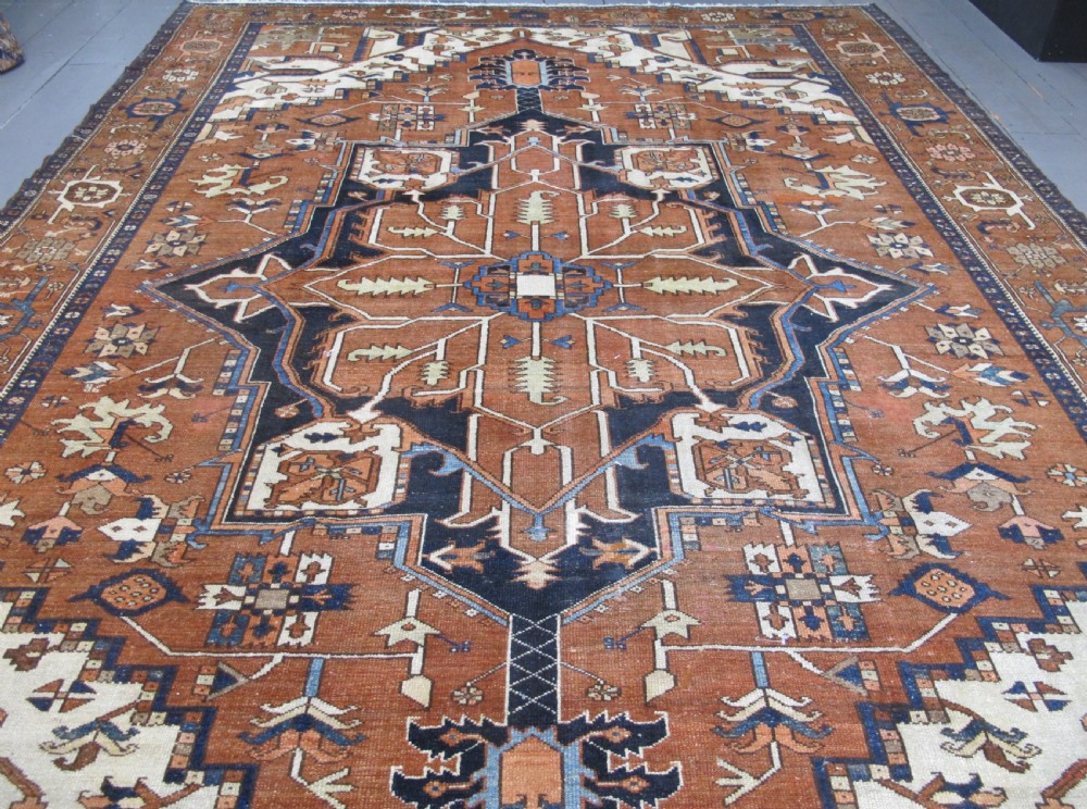 A large 19th-century antique Persian Serapi wool carpet featuring a bold geometric central medallion in navy blue and terracotta on an ivory field with wide decorative borders. View III