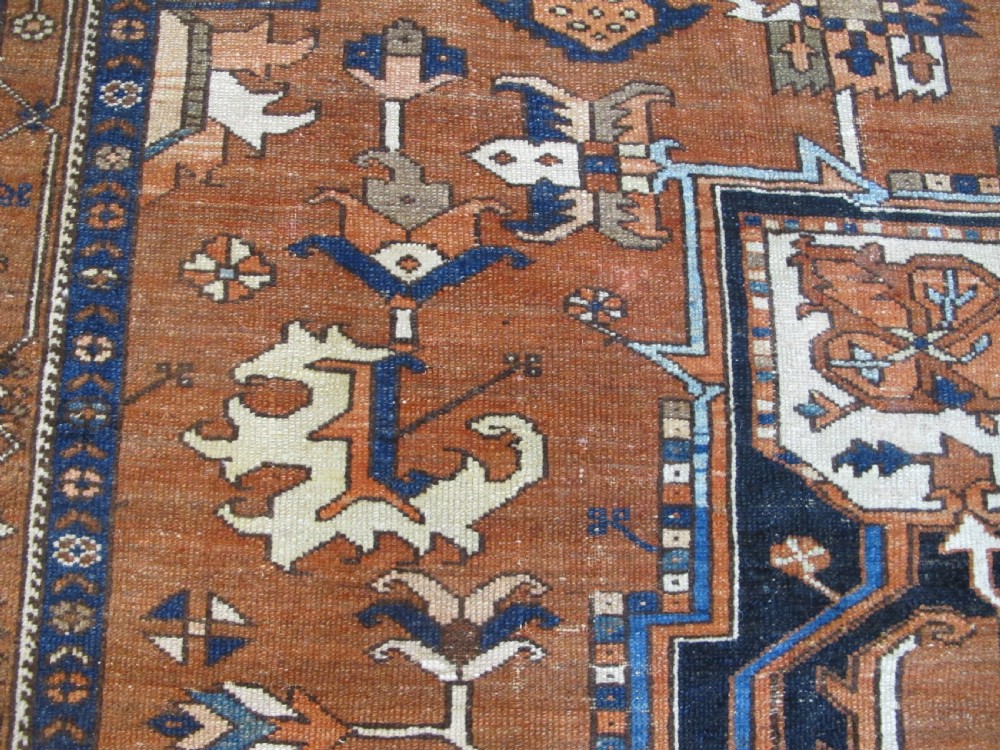 A large 19th-century antique Persian Serapi wool carpet featuring a bold geometric central medallion in navy blue and terracotta on an ivory field with wide decorative borders. View X