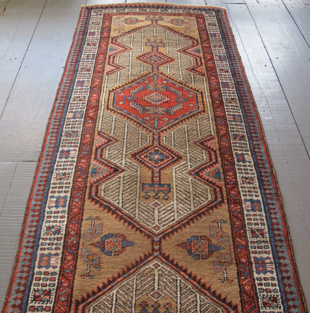 A long and narrow North-West Persian wool runner rug featuring repeating geometric diamond medallions in terracotta, beige, and navy hues. View II