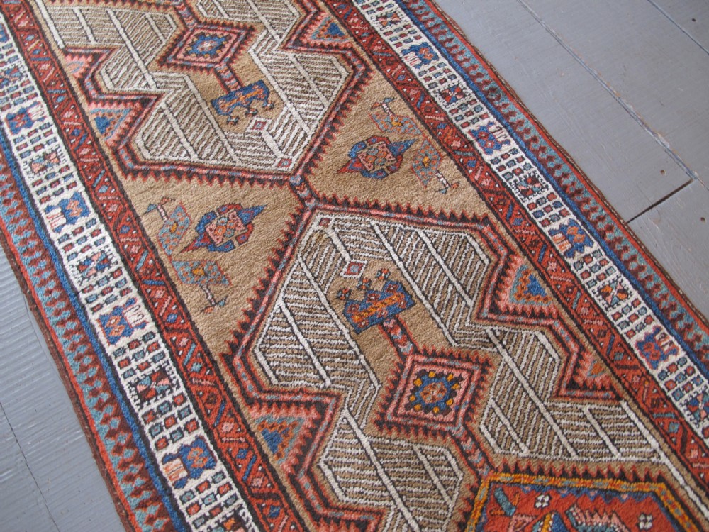 A long and narrow North-West Persian wool runner rug featuring repeating geometric diamond medallions in terracotta, beige, and navy hues. View IV