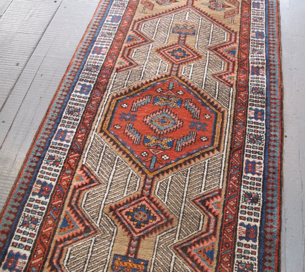 A long and narrow North-West Persian wool runner rug featuring repeating geometric diamond medallions in terracotta, beige, and navy hues. View V