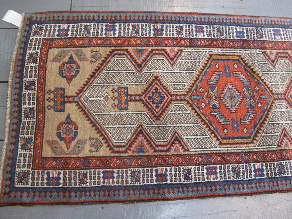 A long and narrow North-West Persian wool runner rug featuring repeating geometric diamond medallions in terracotta, beige, and navy hues. View VI