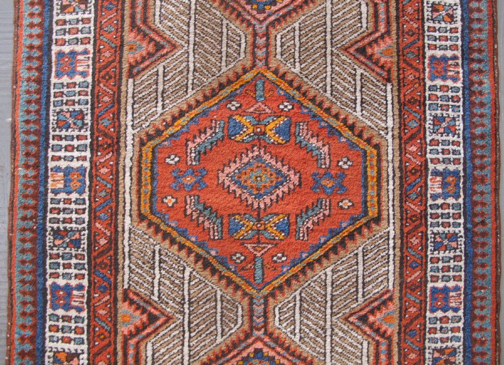 A long and narrow North-West Persian wool runner rug featuring repeating geometric diamond medallions in terracotta, beige, and navy hues. View IX