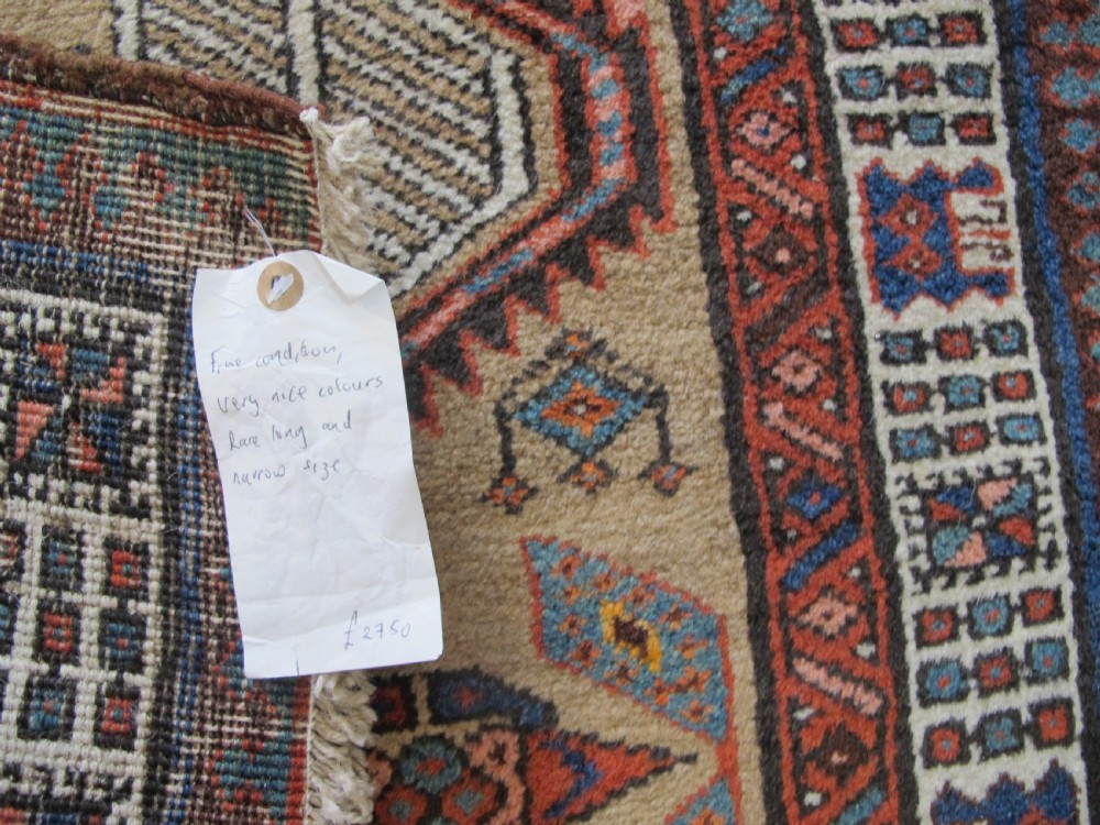 A long and narrow North-West Persian wool runner rug featuring repeating geometric diamond medallions in terracotta, beige, and navy hues. View XI