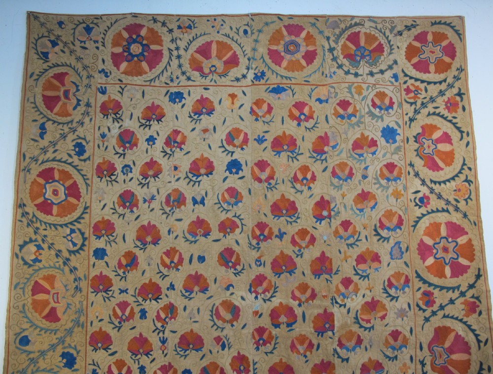 A rectangular 19th-century Bokhara suzani textile featuring hand-embroidered floral rosettes and leaf motifs in red, terracotta, and blue silk threads on a cream cotton field. View II