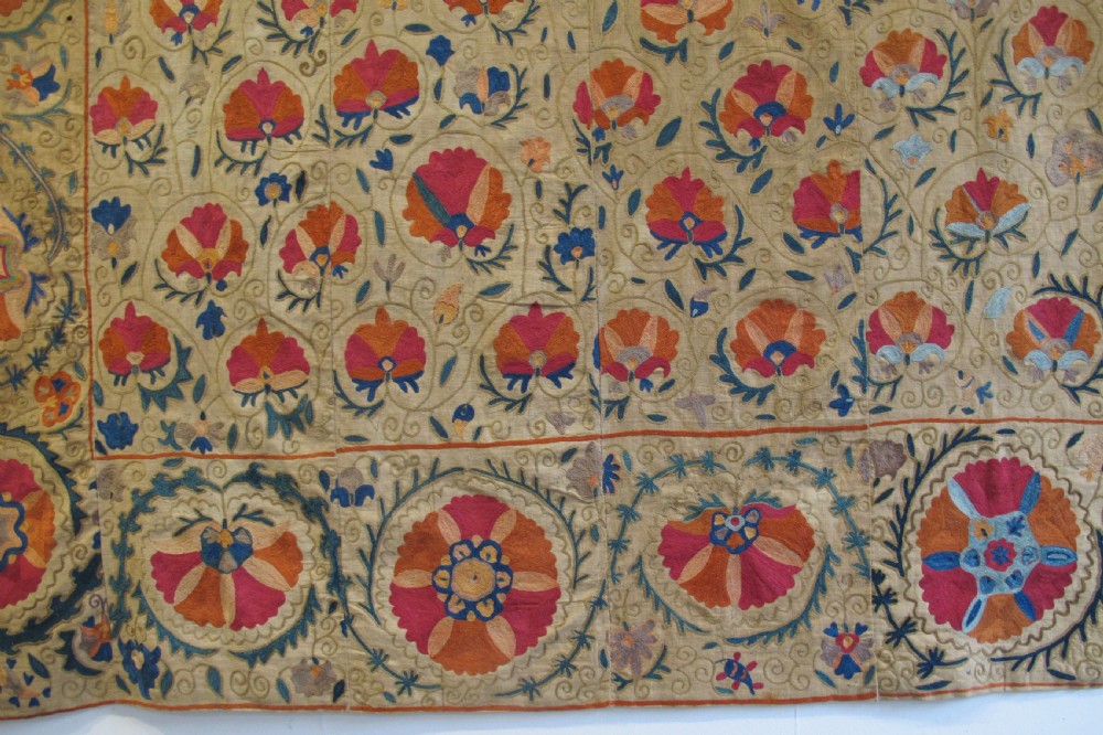 A rectangular 19th-century Bokhara suzani textile featuring hand-embroidered floral rosettes and leaf motifs in red, terracotta, and blue silk threads on a cream cotton field. View III