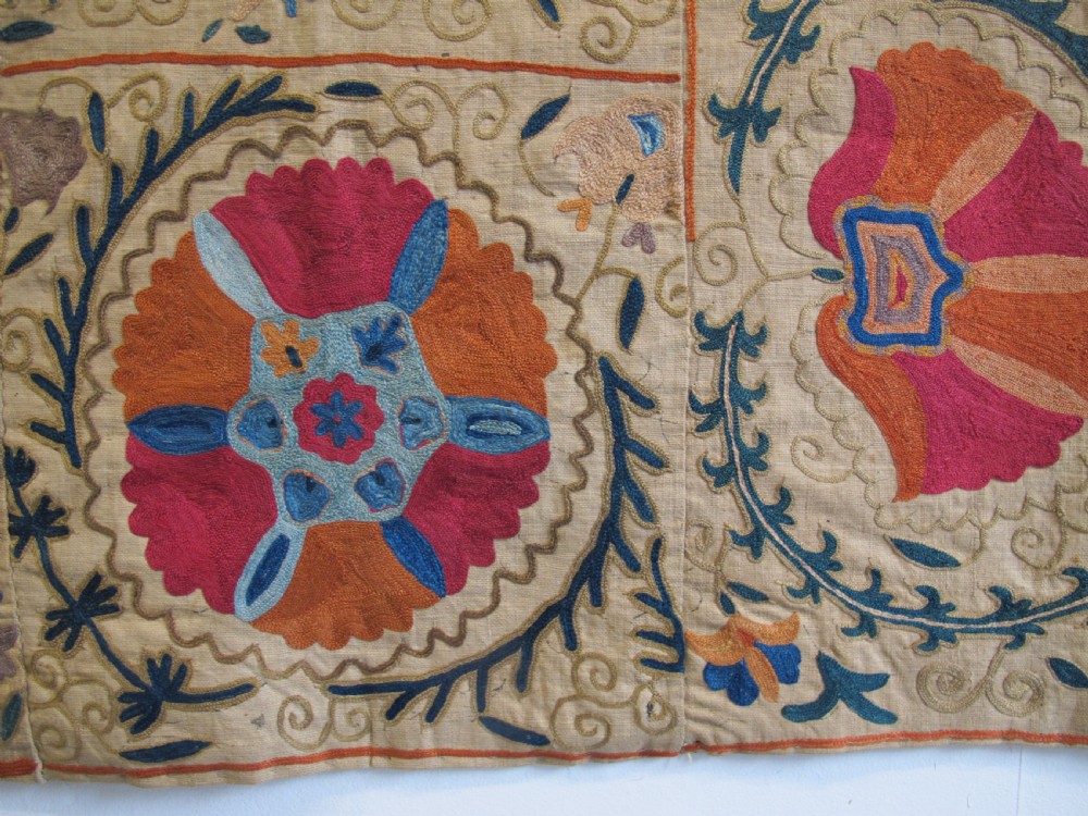 A rectangular 19th-century Bokhara suzani textile featuring hand-embroidered floral rosettes and leaf motifs in red, terracotta, and blue silk threads on a cream cotton field. View IV