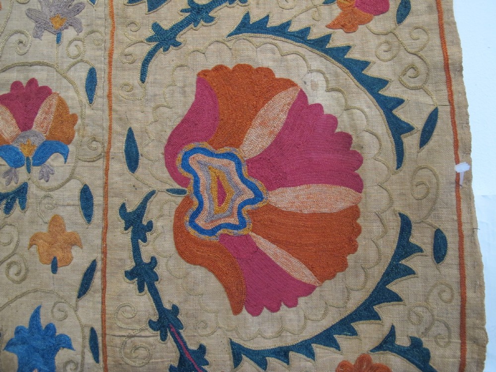 A rectangular 19th-century Bokhara suzani textile featuring hand-embroidered floral rosettes and leaf motifs in red, terracotta, and blue silk threads on a cream cotton field. View V