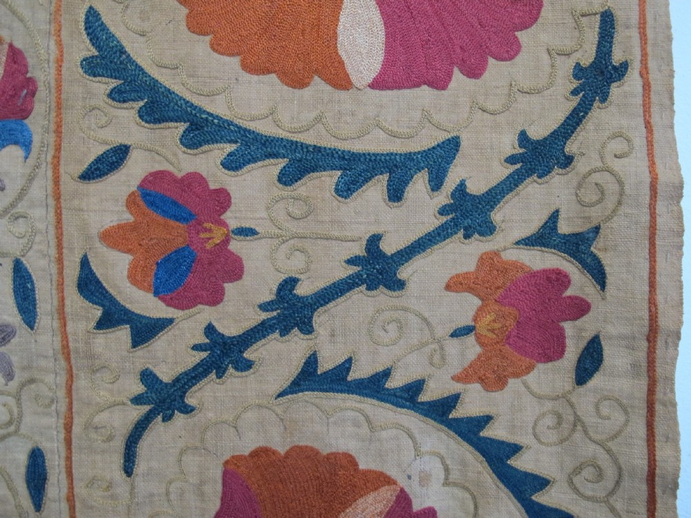 A rectangular 19th-century Bokhara suzani textile featuring hand-embroidered floral rosettes and leaf motifs in red, terracotta, and blue silk threads on a cream cotton field. View VI