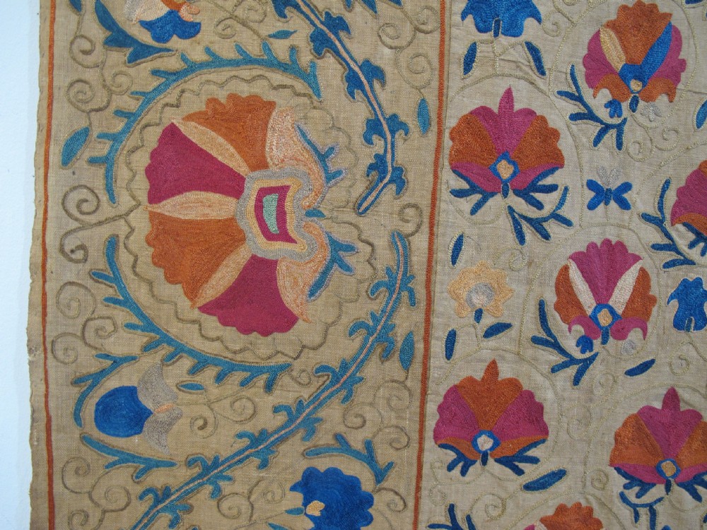 A rectangular 19th-century Bokhara suzani textile featuring hand-embroidered floral rosettes and leaf motifs in red, terracotta, and blue silk threads on a cream cotton field. View VII