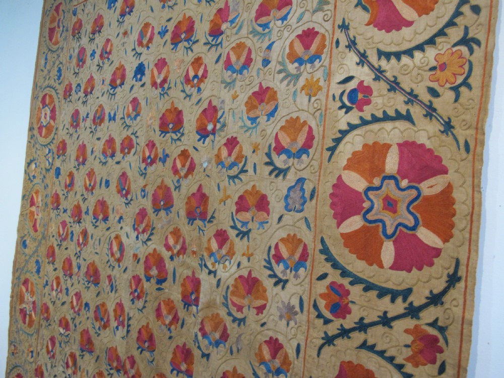 A rectangular 19th-century Bokhara suzani textile featuring hand-embroidered floral rosettes and leaf motifs in red, terracotta, and blue silk threads on a cream cotton field. View XI