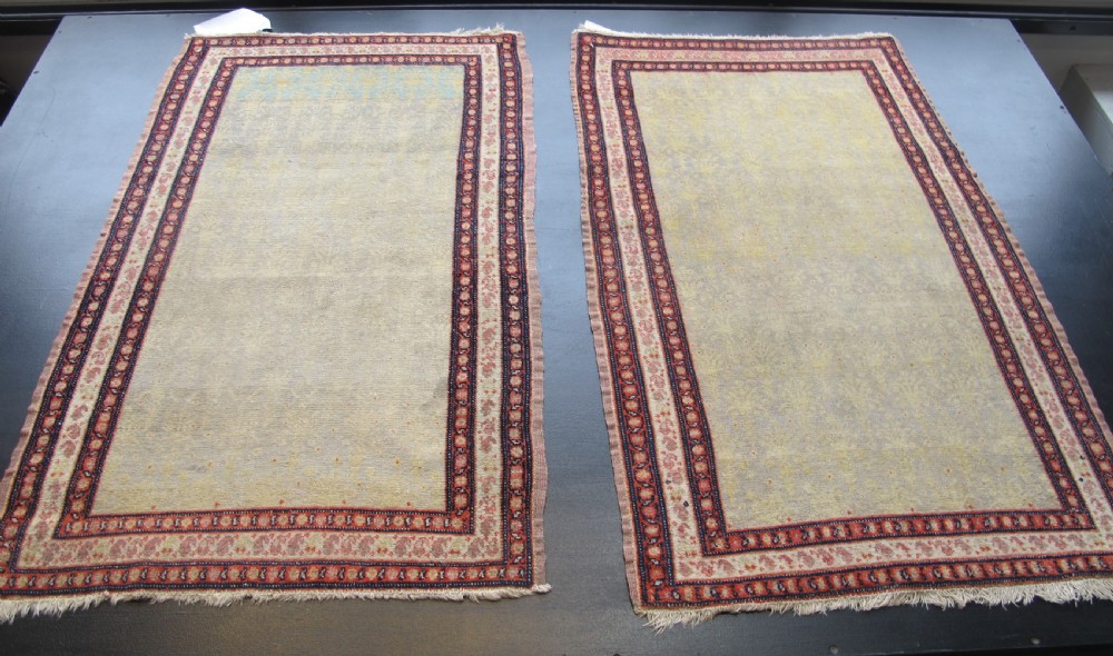 A pair of late nineteenth-century Persian Senneh hand-knotted wool rugs featuring pale cream central fields and multi-stripe red borders.