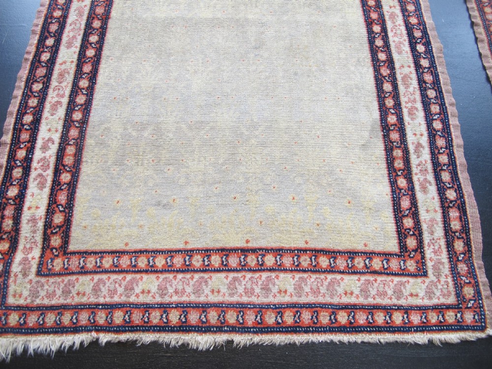 A pair of late nineteenth-century Persian Senneh hand-knotted wool rugs featuring pale cream central fields and multi-stripe red borders. View V
