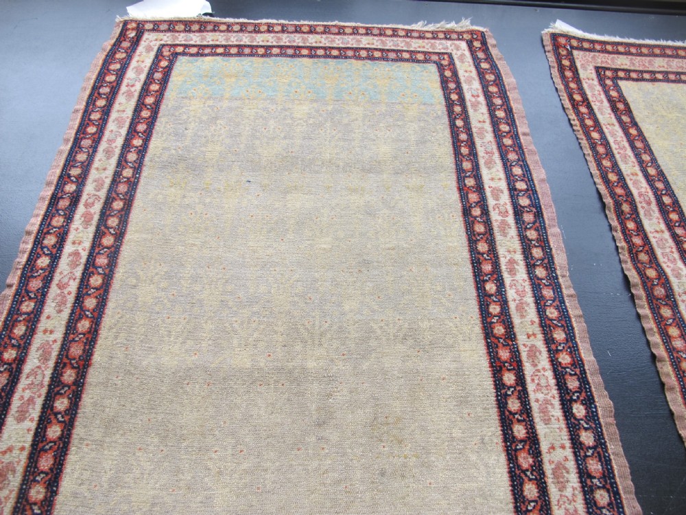 A pair of late nineteenth-century Persian Senneh hand-knotted wool rugs featuring pale cream central fields and multi-stripe red borders. View VI