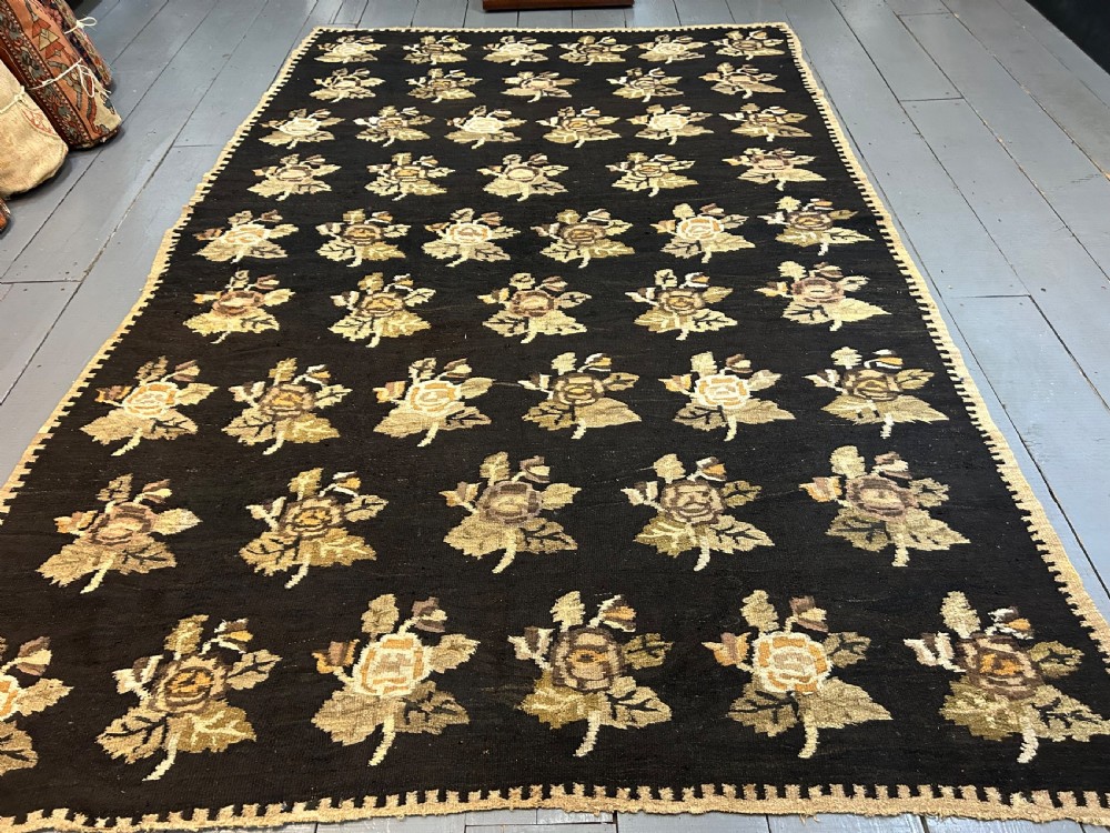 A large flat-woven Ukrainian wool kilim featuring a dark brown background decorated with repeating beige and mustard floral motifs.
