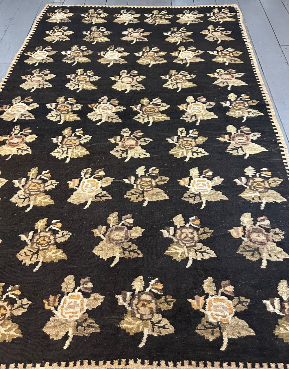 A large flat-woven Ukrainian wool kilim featuring a dark brown background decorated with repeating beige and mustard floral motifs. View XII