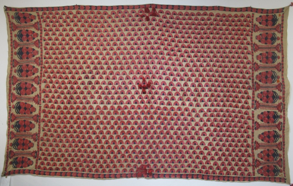An antique rectangular Sindh embroidered textile featuring a repeating red arched pattern on a beige ground with decorative borders and tassels.