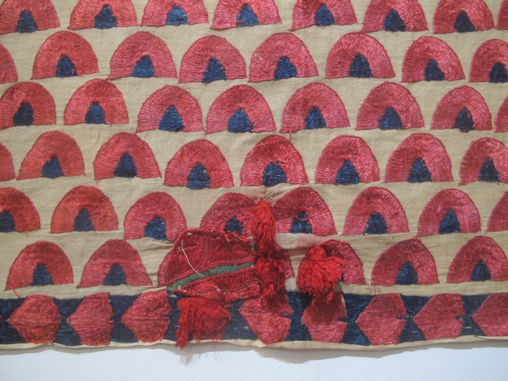 An antique rectangular Sindh embroidered textile featuring a repeating red arched pattern on a beige ground with decorative borders and tassels. View V