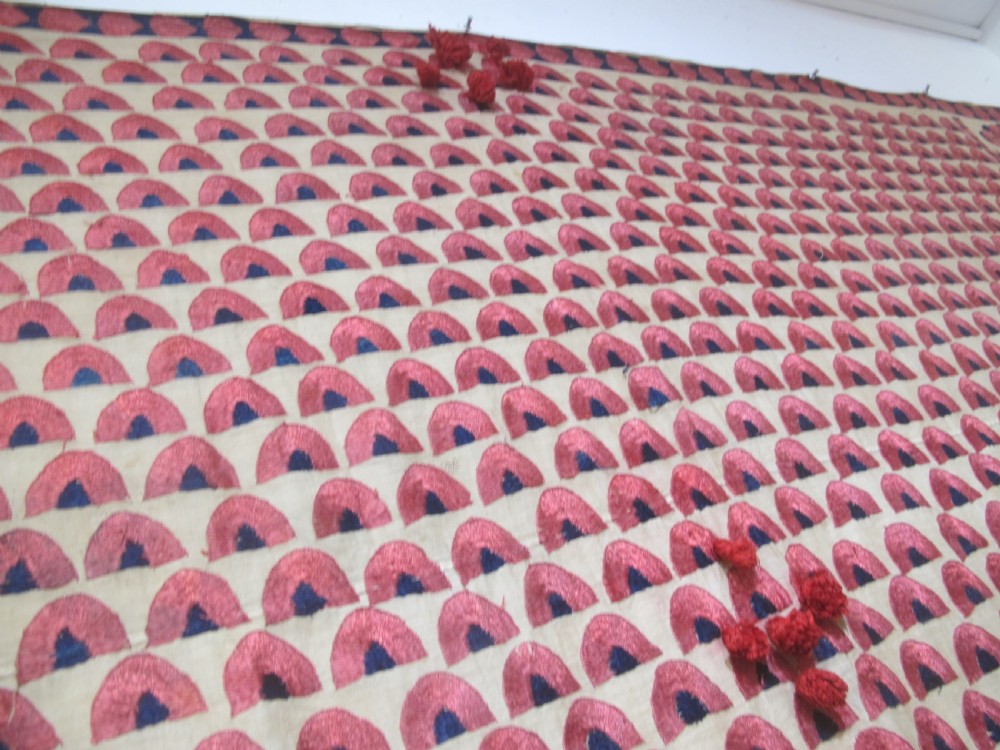 An antique rectangular Sindh embroidered textile featuring a repeating red arched pattern on a beige ground with decorative borders and tassels. View X