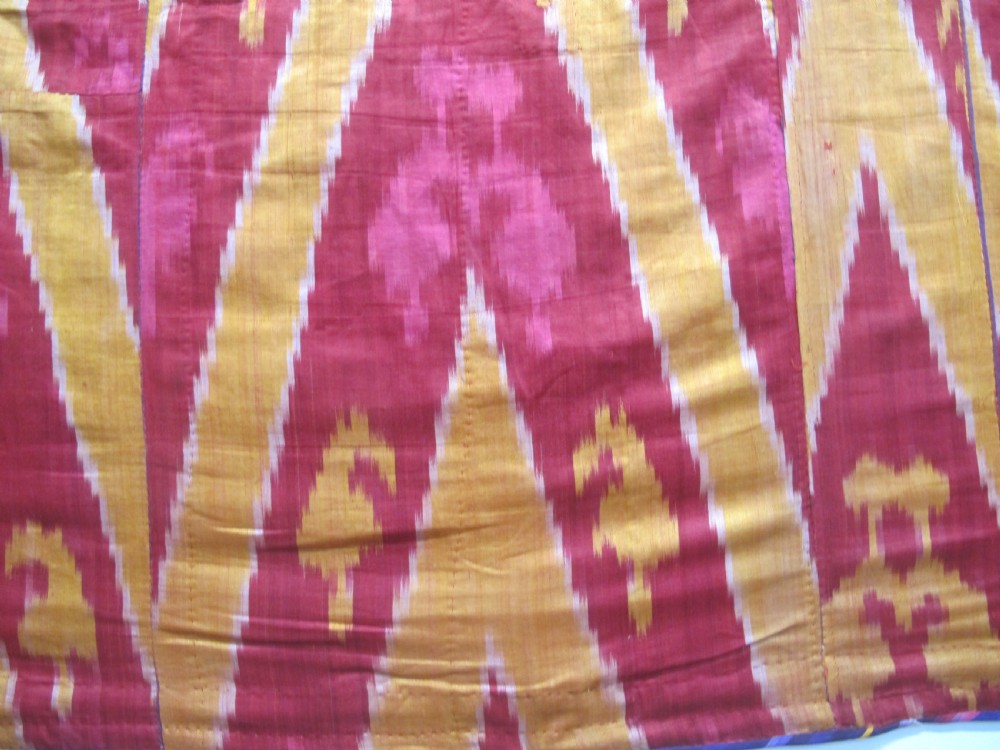 A rectangular handwoven silk ikat textile panel featuring large geometric chevron and diamond patterns in red, yellow, and magenta hues. View II