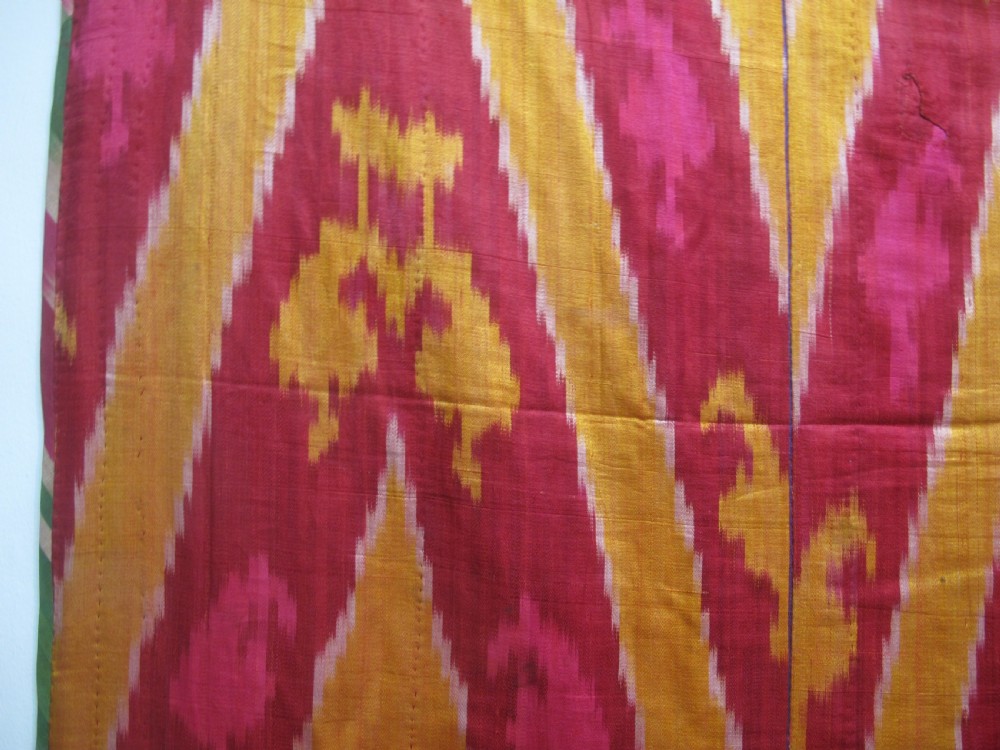 A rectangular handwoven silk ikat textile panel featuring large geometric chevron and diamond patterns in red, yellow, and magenta hues. View III