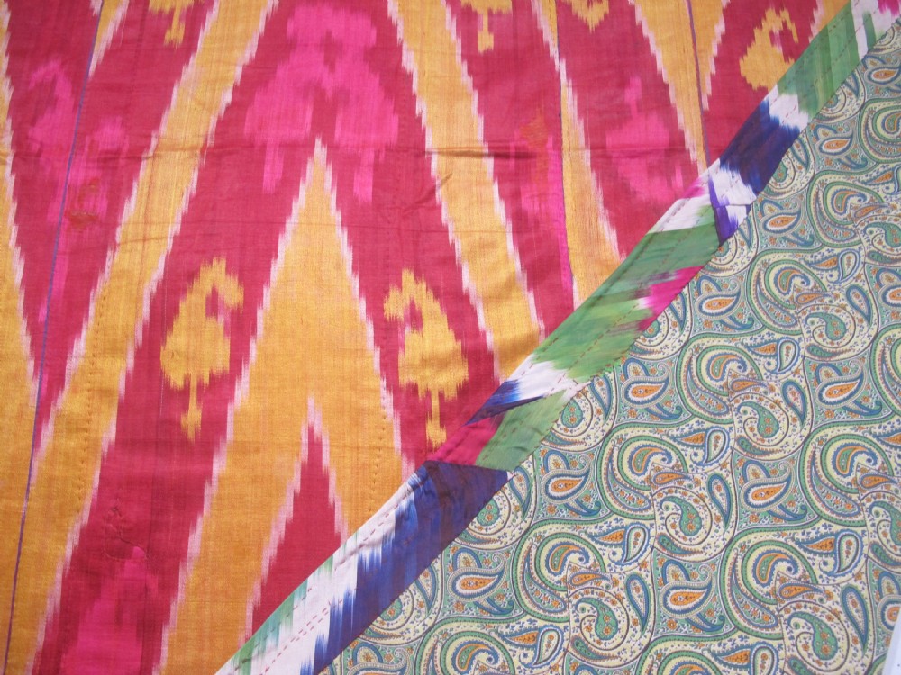 A rectangular handwoven silk ikat textile panel featuring large geometric chevron and diamond patterns in red, yellow, and magenta hues. View V