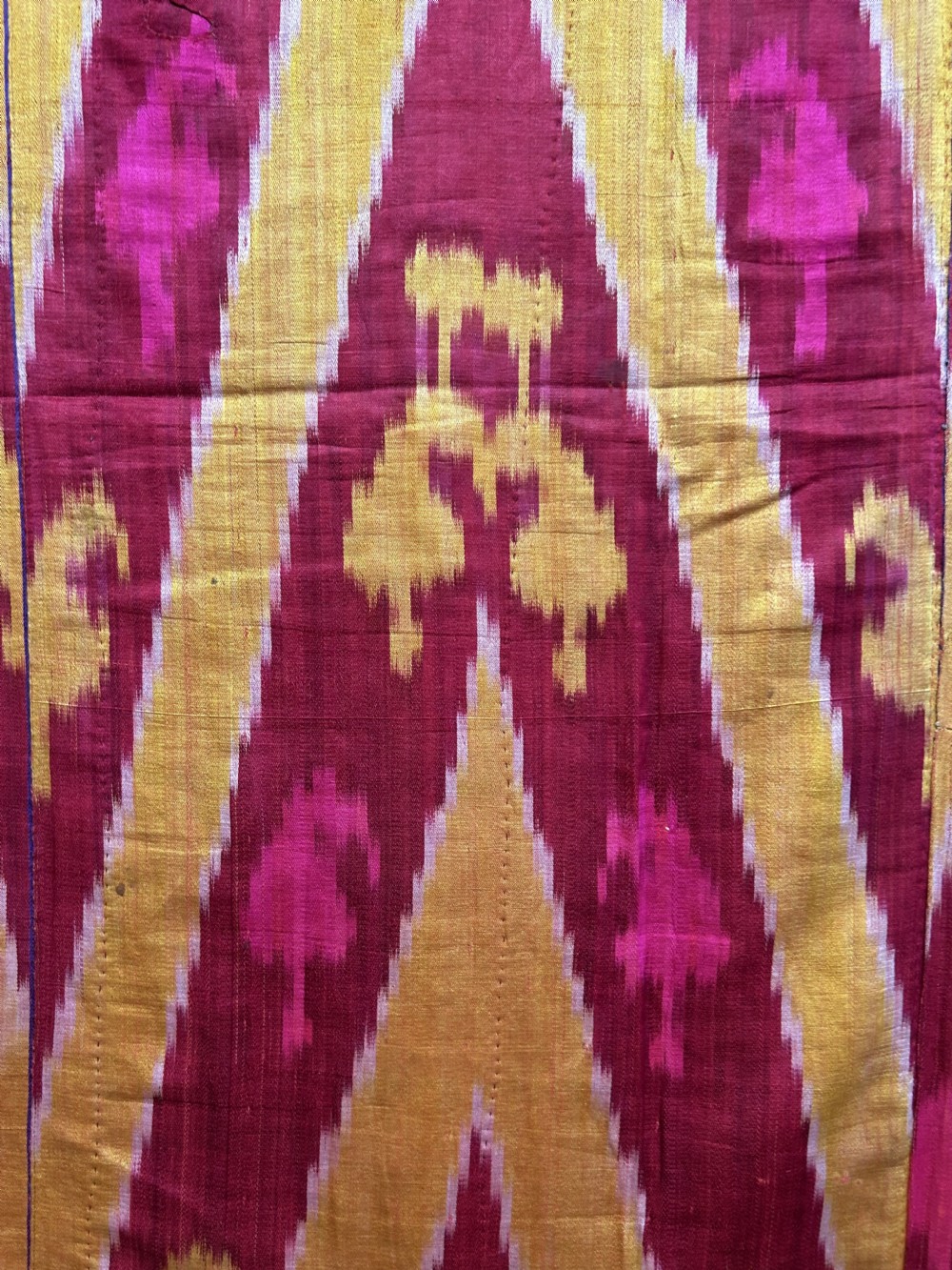 A rectangular handwoven silk ikat textile panel featuring large geometric chevron and diamond patterns in red, yellow, and magenta hues. View VI