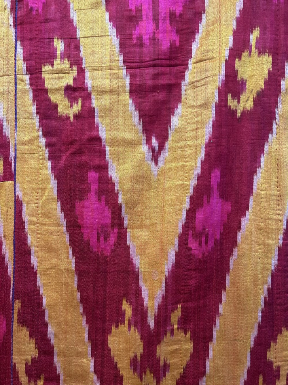 A rectangular handwoven silk ikat textile panel featuring large geometric chevron and diamond patterns in red, yellow, and magenta hues. View VII