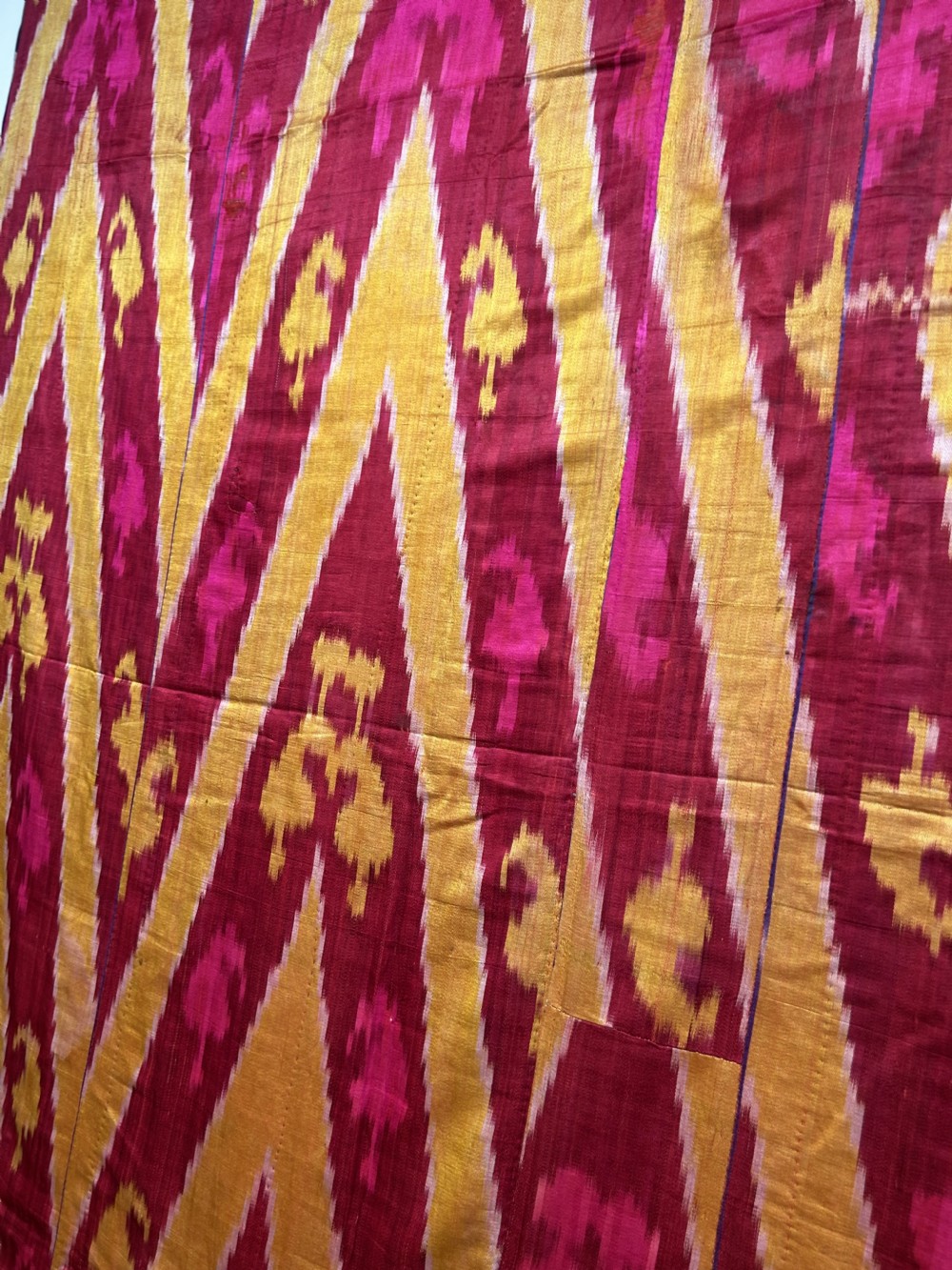 A rectangular handwoven silk ikat textile panel featuring large geometric chevron and diamond patterns in red, yellow, and magenta hues. View IX