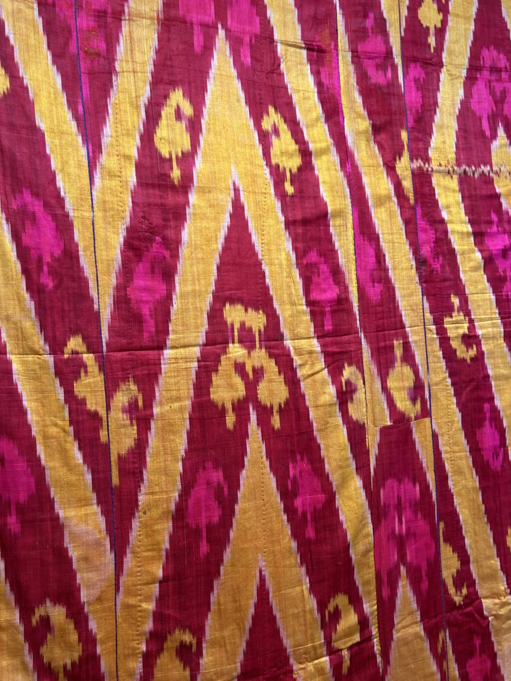 A rectangular handwoven silk ikat textile panel featuring large geometric chevron and diamond patterns in red, yellow, and magenta hues. View X