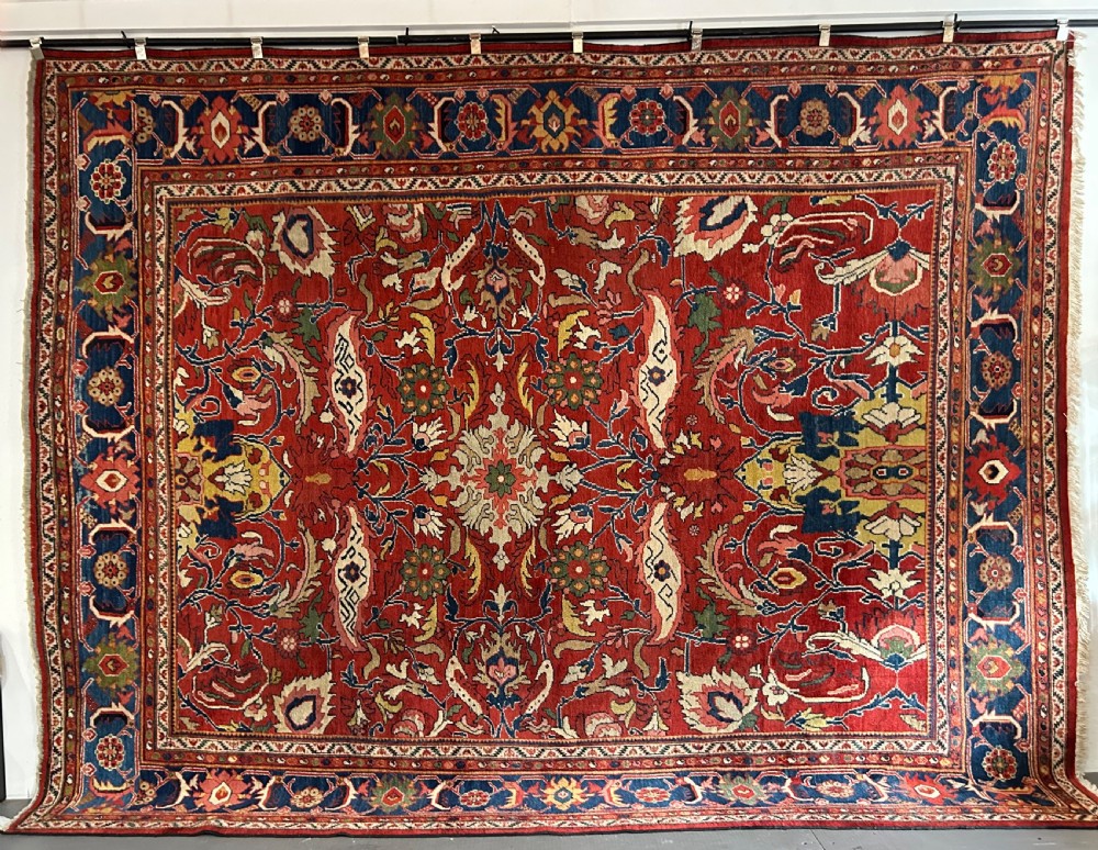 A large 19th-century Persian Sultanabad hand-knotted wool carpet featuring a rich red central field decorated with intricate botanical palmettes surrounded by a wide dark blue patterned border.