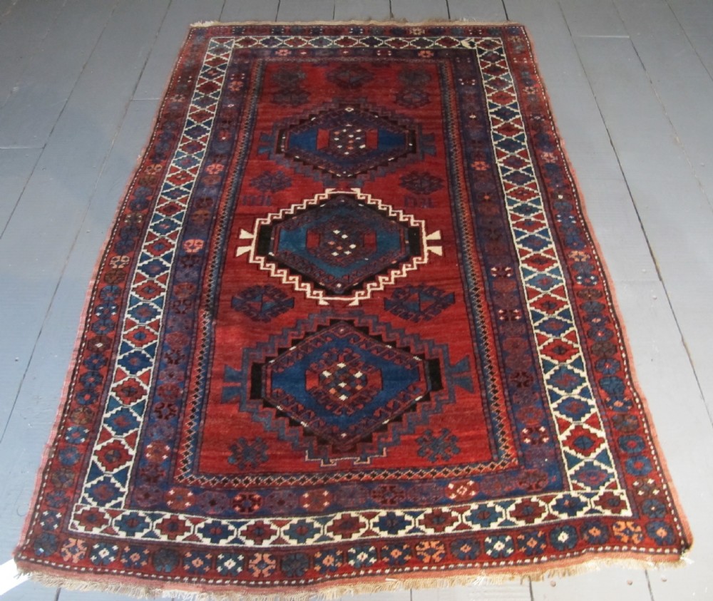 A hand-knotted Caucasian Kazak wool rug featuring three central geometric diamond medallions on a red field framed by patterned borders.