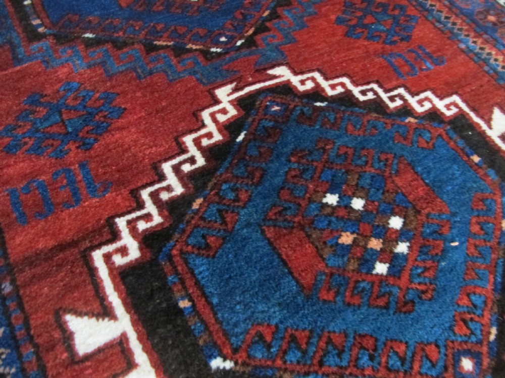 A hand-knotted Caucasian Kazak wool rug featuring three central geometric diamond medallions on a red field framed by patterned borders. View III