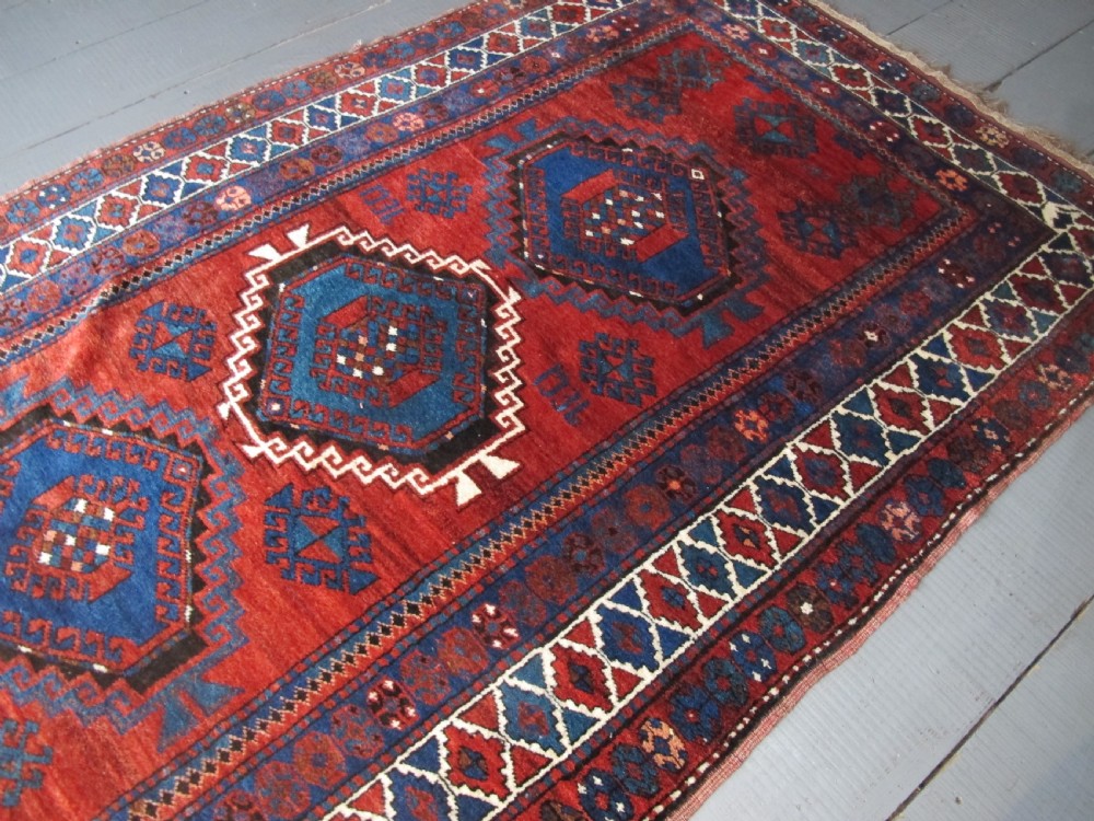 A hand-knotted Caucasian Kazak wool rug featuring three central geometric diamond medallions on a red field framed by patterned borders. View IV