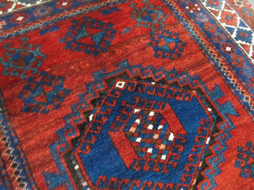 A hand-knotted Caucasian Kazak wool rug featuring three central geometric diamond medallions on a red field framed by patterned borders. View V