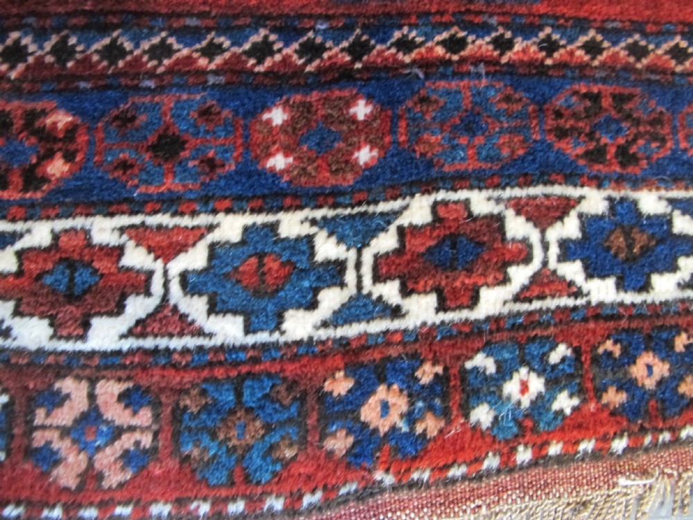 A hand-knotted Caucasian Kazak wool rug featuring three central geometric diamond medallions on a red field framed by patterned borders. View VII