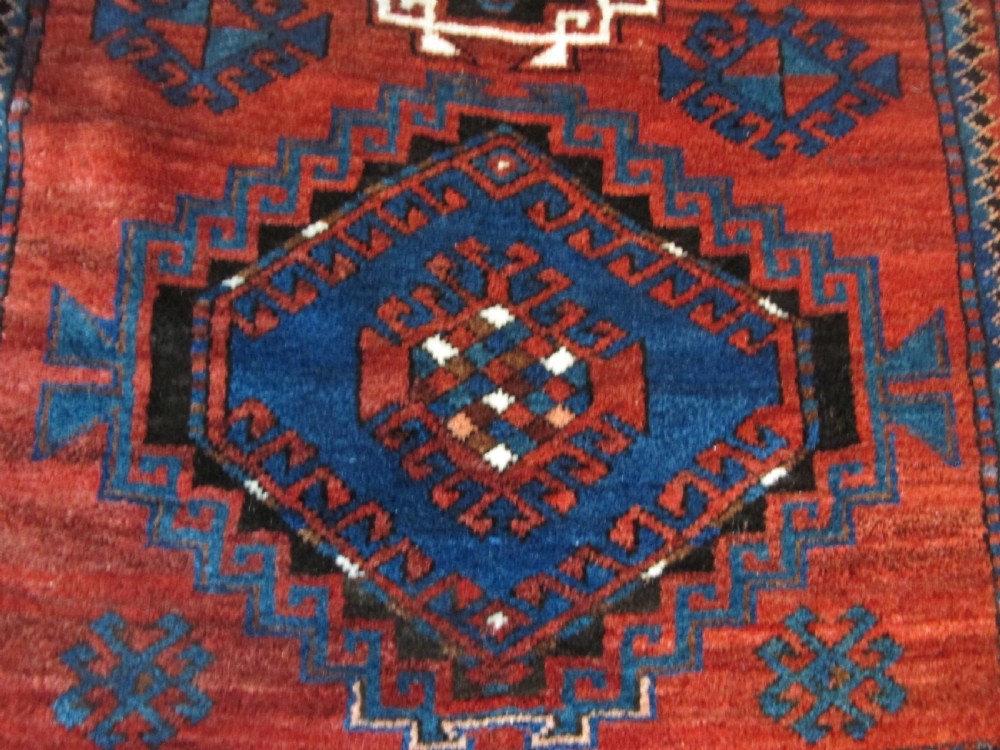 A hand-knotted Caucasian Kazak wool rug featuring three central geometric diamond medallions on a red field framed by patterned borders. View VIII