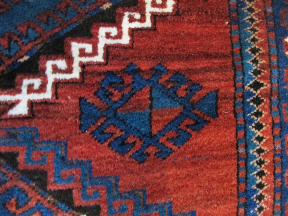 A hand-knotted Caucasian Kazak wool rug featuring three central geometric diamond medallions on a red field framed by patterned borders. View IX