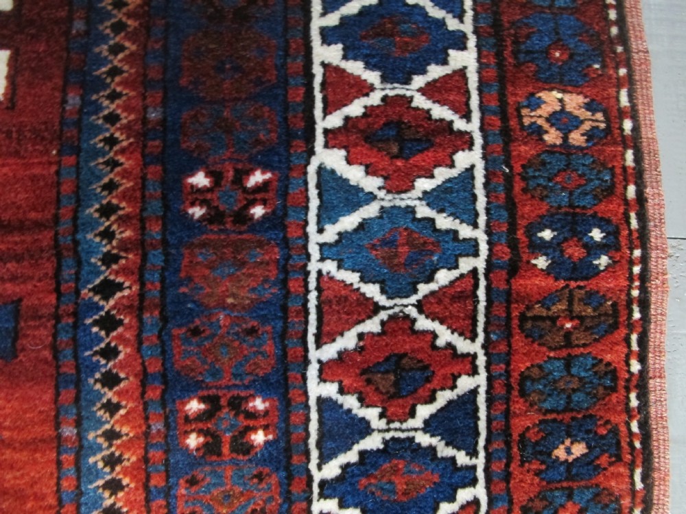 A hand-knotted Caucasian Kazak wool rug featuring three central geometric diamond medallions on a red field framed by patterned borders. View X