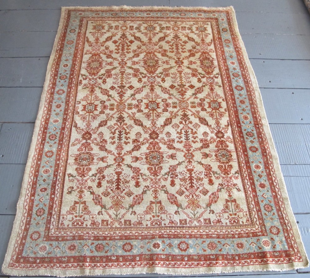 An antique Persian Ziegler wool rug featuring a repeating soft terracotta and light blue floral pattern across an ivory field, bordered by a decorative floral band.